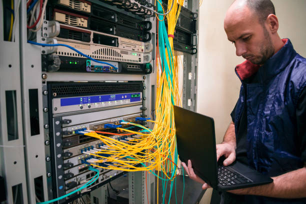 o administrador do sistema com um laptop está na sala do servidor. um homem monta um roteador central em um datacenter. configuração de hardware do servidor. - network server data center installing - fotografias e filmes do acervo