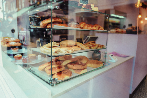 Large selection of cakes and other baked pastries arranged nicely and on display in a bakery shop window.