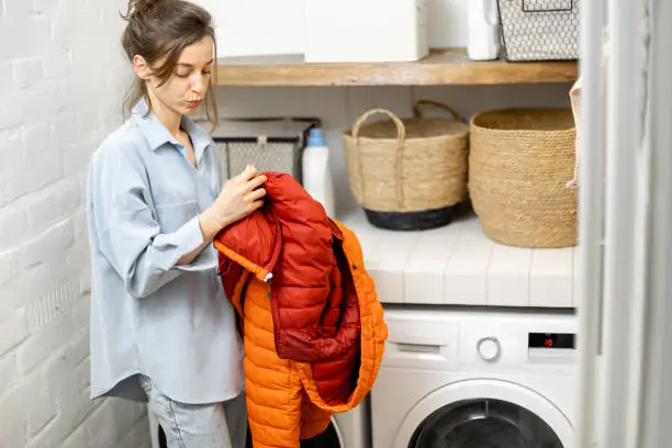 Young housewife looks on a down jacket before washing it in the laundry at home. Manual or automatic washing of outerwear from down