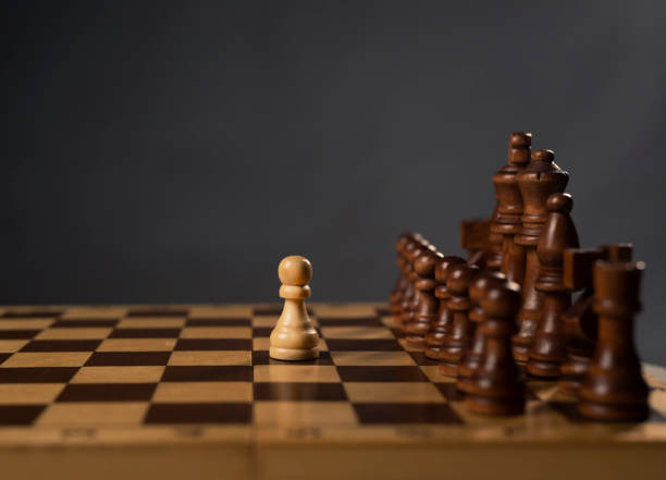 istock One white pawn against group of black chess figures on chessboard. Brave decisions concept 1308259146