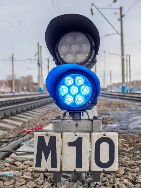 Dwarf railway traffic light with blue-light signal standing near the railway tracks.