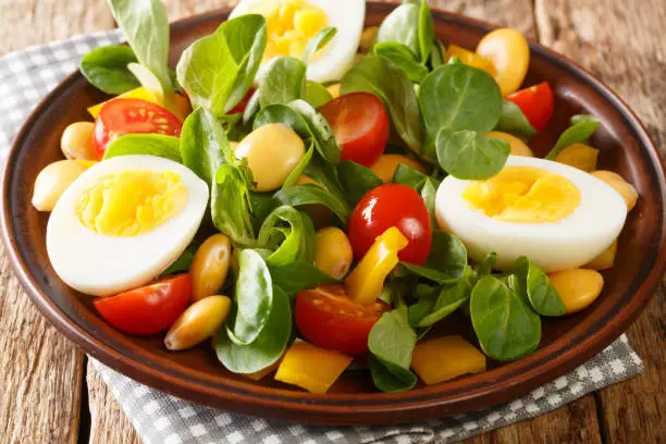 Vitamin delicious salad of lupine beans, boiled eggs, tomatoes and common cornsalad close-up in a plate on the table. horizontal