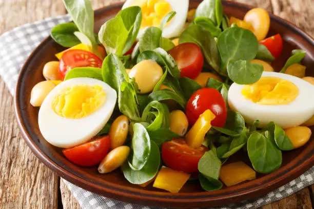 Breakfast of boiled eggs and salad of lupine beans, tomatoes and common cornsalad close-up in a plate on the table. horizontal