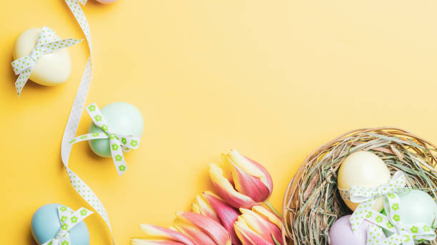 istock Easter egg. Happy Easter decoration: Colourful egg with tape ribbon, spring tulips, white feathers on pastel yellow background. Traditional decoration in sun light. Top view. 1308265050