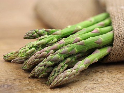 Horizontal closeup photo of a bunch of organic green Asparagus lying on a weathered pale blue painted wooden table in Spring.