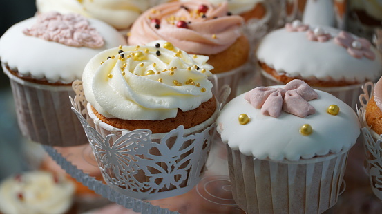 Stock photo showing close-up, elevated view of bakery shelf display of individual cupcakes in silver paper cake cases available for purchasing.