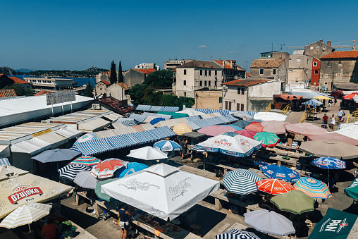 cityscape of Šibenik, Croatia with market stands under colorful parasols in the foreground