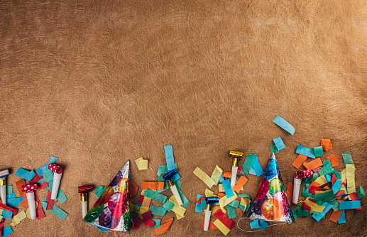 Multi-colored confetti, party hats and party horn blowers on brown background. Flat lay concept.