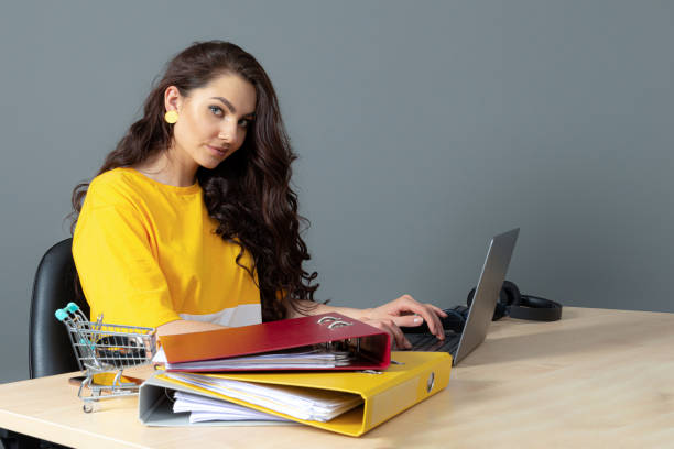 jeune femme d’affaires avec le long cheveu foncé travaillant avec le document dans le bureau, isolé sur le fond gris - paper document pen long hair photos et images de collection