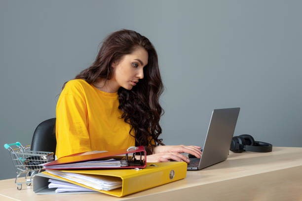 jeune femme d’affaires avec le long cheveu foncé travaillant avec le document dans le bureau, isolé sur le fond gris - paper document pen long hair photos et images de collection