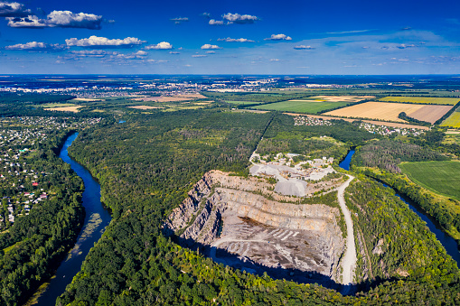 Top view of a stone, granite quarry. Beautiful forest, blue sky, clouds. River flows. Green fields on top.