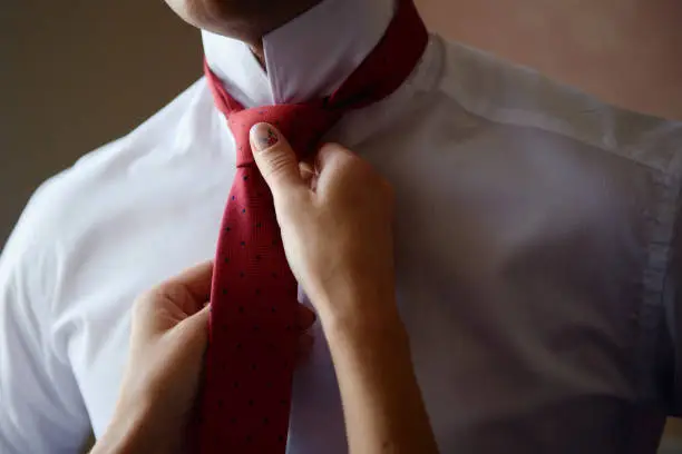 Woman helping her husband to fixing red necktie, close up