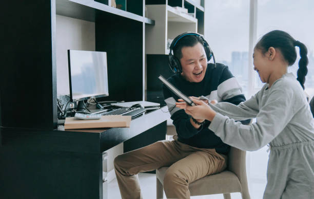 mischief asian chinese daughter distracting playing disturbing her father who working from home routine with headset videocall with his colleague coworking - inconvenience meeting business distracted imagens e fotografias de stock