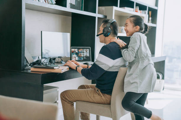 mischief asian chinese daughter distracting playing disturbing her father who working from home routine with headset videocall with his colleague coworking - inconvenience meeting business distracted imagens e fotografias de stock