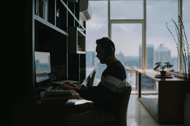 シルエットサイドビューアジアの中国人成熟した男性は、彼の同僚とリビングルームのビデオ通話で自宅から働く - working at home headset telecommuting computer ストックフォトと画像