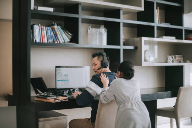 mischief asian chinese daughter distracting playing disturbing her father who working from home routine with headset videocall with his colleague coworking - inconvenience meeting business distracted imagens e fotografias de stock