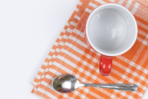 Top view of empty cup for coffee with spoon on the dishcloth with copy space above white background.