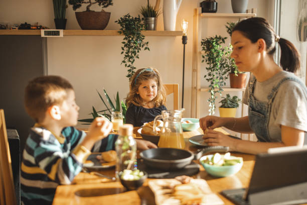 istock Two kids with their mother sitting at table during breakfast 1308287876