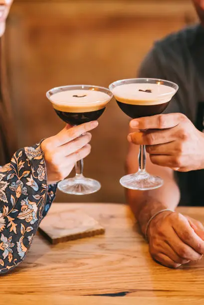 couple holding glass with espresso martini cocktail, decorated with coffee bean.