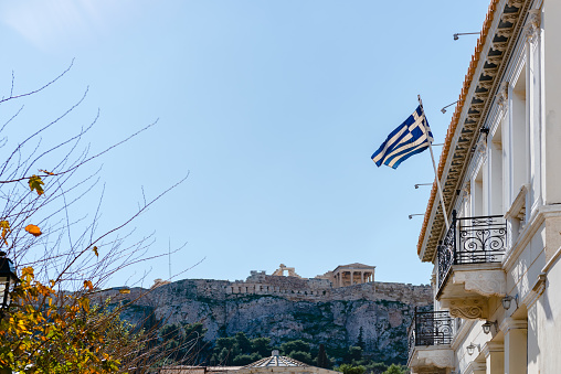 Greek flag on balcony against the Parthenon of Athenian Acropolis.