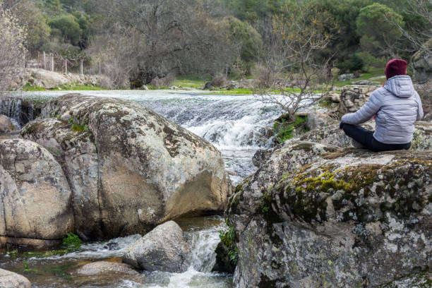 Girl with silver jacket relaxed in nature next to a waterfall in the river