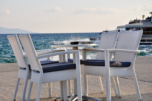 Beach cafe with sea view at sunset, empty table, four chairs, vacant for guests. Simple, white wooden furniture. Beautiful summer holiday concept. Horizon with misty mountains on distant island.
