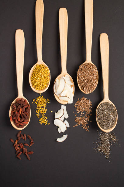 vista dall'alto di diversi tipi di superfood naturali nei cucchiai di legno sullo sfondo nero - wolfberry seed wooden spoon spoon foto e immagini stock