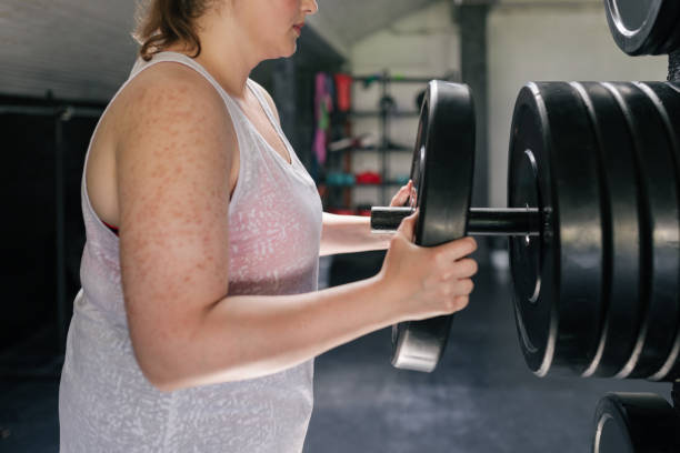 istock Strength Workouts: an  Plus Size Woman Taking a Disk Weight from the Rack 1308296337