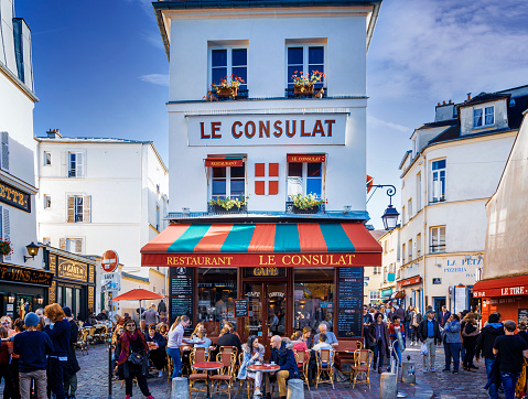 People sitting outside restaurant Le Consulat at Montmartre Paris. Manu people walk in the streets. Montmartre is a must see for all tourists coming to Paris