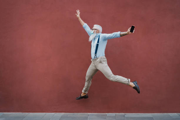 istock Senior crazy man jumping outdoors while wearing mask with red wall in background - Focus on face 1308301654