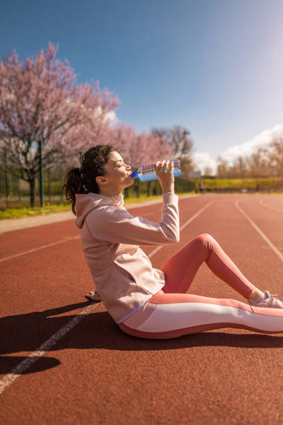 joven deportiva bebiendo agua después de correr en pista deportiva. - running track women running spring fotografías e imágenes de stock