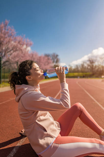 joven deportiva bebiendo agua después de correr en pista deportiva. - running track women running spring fotografías e imágenes de stock