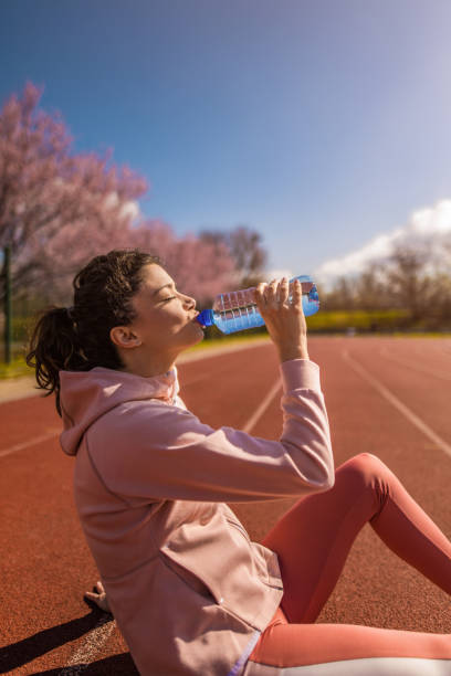 joven deportiva bebiendo agua después de correr en pista deportiva. - running track women running spring fotografías e imágenes de stock