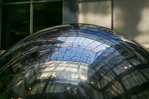 Close-up view. Distorted glass roof of modern building reflects in metal mirror sphere. Abstract architecture background.