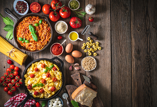 Italian food pasta recipes and ingredients as and tomato and mozzarella fusilli and spaghetti with tomato on rustic wood table  in cast iron pan