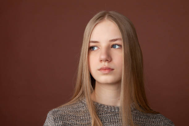 Studio portrait of blonde teenage girl Close up studio portrait of blonde teenage girl with long hair in gray sweater on brown background 15 year old blonde girl stock pictures, royalty-free photos & images
