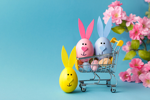 Shopping cart, Eeaster eggs bunny, flowers on blue background, copy space. sale concept