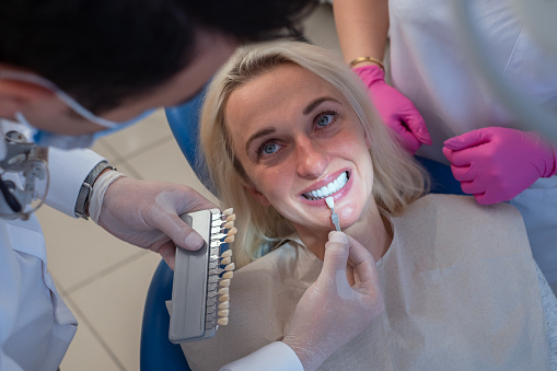 Dentist uses a palette tooth color sample to determine shade of patient's female teeth.