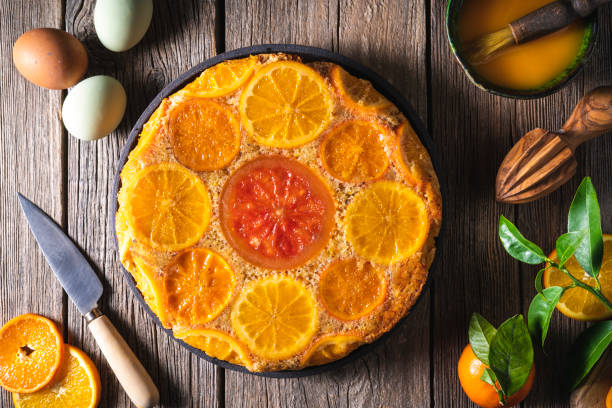Orange citrus upside down cake with ingredients as citrus slices, juice, eggs, on rustic wooden table