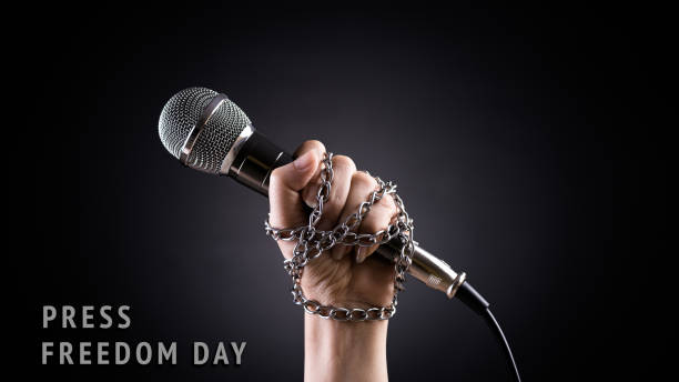 istock World press freedom day concept. Hand holding a microphone with chain on dark background, symbol of press freedom or speech freedom. 1308324149