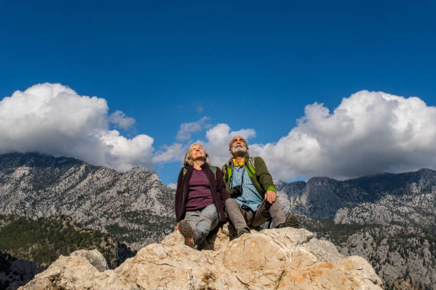 Elderly couple, positive expression, sitting on high rocks, enjoying nature.