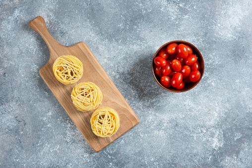 Pasta nest on wooden board with bowl of tomatoes. High quality photo