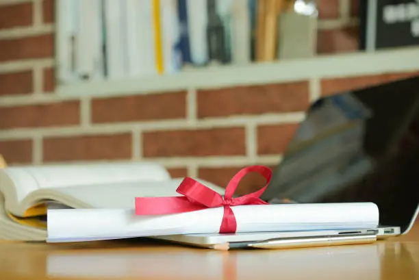 Photo of close up bachelor's degree certificate on laptop with book in the library for online learning graduation concept