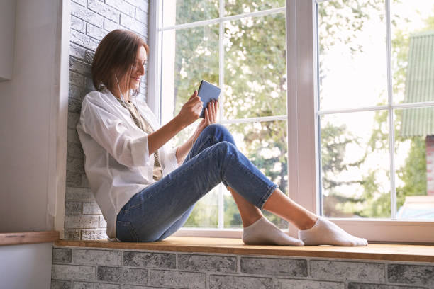 Young woman sitting at windowsill. Working on tablet. Online study concept.