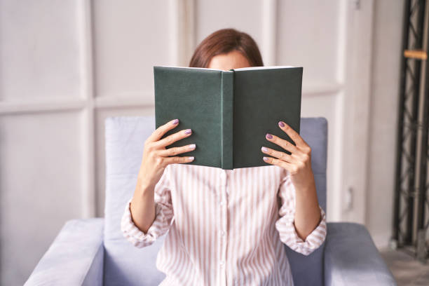 Young woman sitting at chair. Hide face behind notebook Young woman sitting at chair. Hide face behind notebook. Study concept. Safety lockdown distance teaching. Female person. Quarantine office. Business writer unconventional wisdom stock pictures, royalty-free photos & images