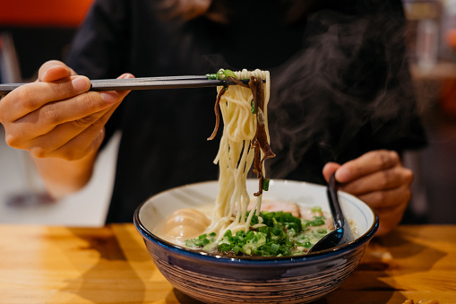 Close up of hand of an Asian woman eating a bowl of Japanese ramen using chopsticks in a Japanese ramen shop