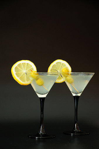 Two glasses of martini with olives and lemon slices on a black background. Close-up.