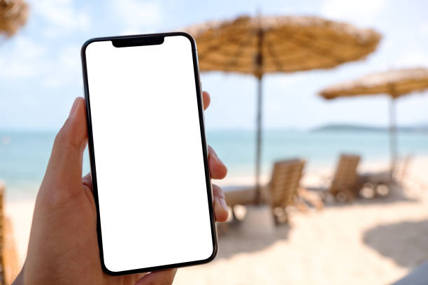 a man holding mobile phone with blank desktop screen while sitting on the beach