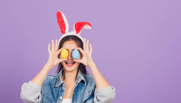 istock woman smiling wearing rabbit ears and denims holding colorful Easter eggs front eyes 1308362440