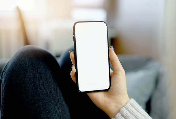 istock Back view close up of a woman hand holding and using smart phone with white blank empty screen sitting on a bed at home. 1308363846